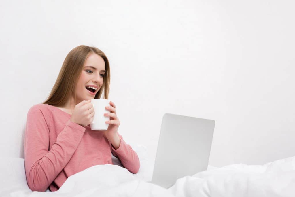 Happy Woman In Bed With A Coffee And Laptop