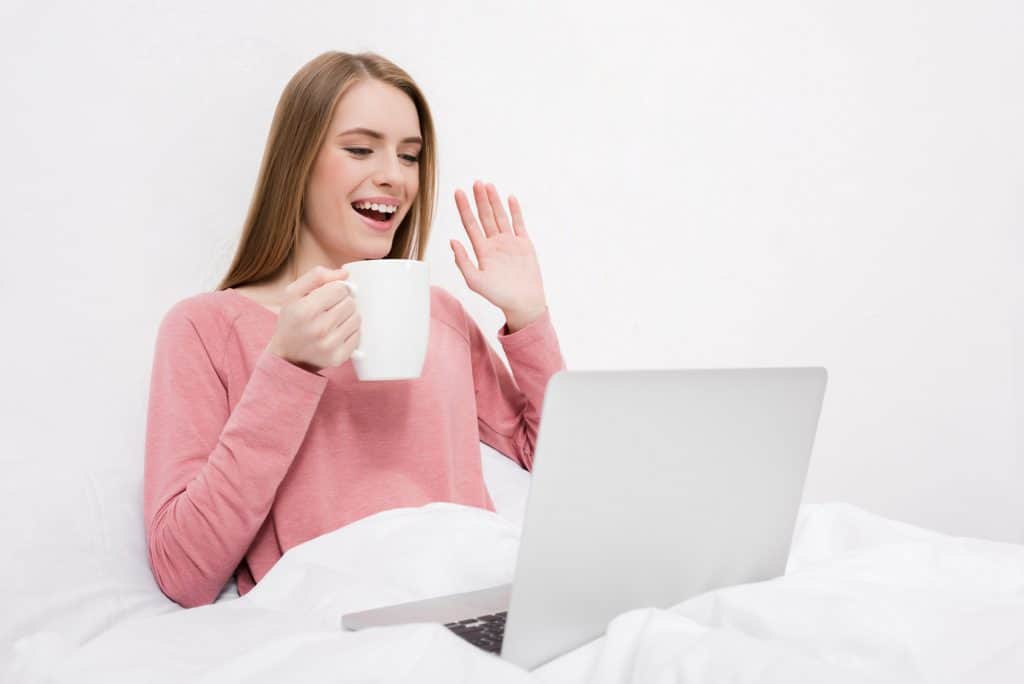 Woman In Bed With Her Laptop Holding A Cup